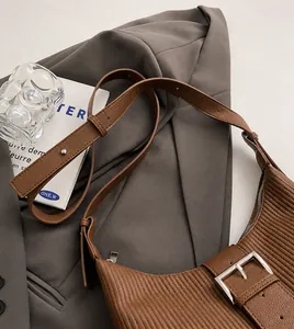 Close-up of brown textured leather shoulder bag with adjustable strap and metal buckle