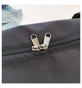 Détail de la double fermeture éclair en métal sur un sac bandoulière noir en toile
