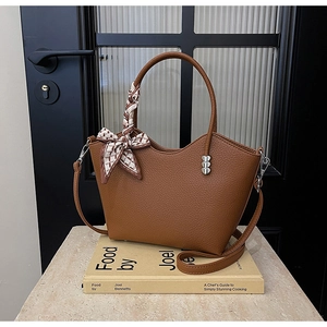 Détail d'un sac en cuir grainé marron avec clous en forme de cœur et poignée en foulard