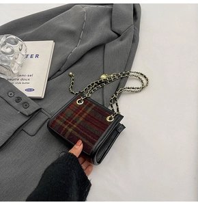 Detail der rot-grün karierten Mini-Umhängetasche mit Goldkette auf grauem Sakko