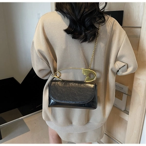 Detalle de bolso bandolera negro brillante con asa grande de imperdible dorado y cadena