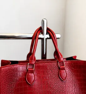 Close-up of red crocodile pattern leather tote bag with sturdy handles and metal rings