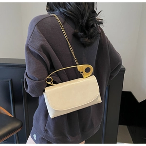 Detalle de bolso minimalista en piel sintética beige con asa de imperdible dorado y cadena
