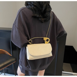 Detalle de bolso beige con asa de imperdible dorado y correa de cadena fina metálica
