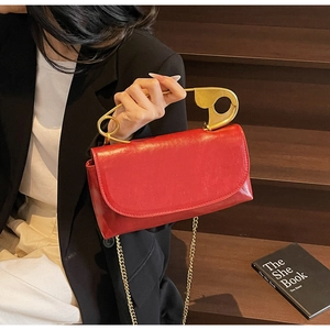 Dettaglio della borsa in pelle lucida rossa con manico creativo a spilla da balia dorata