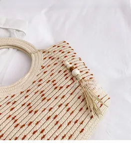 Détail du sac seau tressé beige avec pois marrons et pompons aux perles de bois