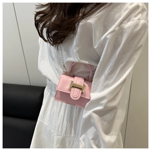 Detailed shot of pink crossbody bag with gold metal hardware and chain on a white dress