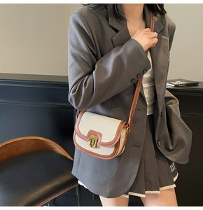 Close-up of retro saddle bag with cream canvas, brown leather trim, and gold buckle