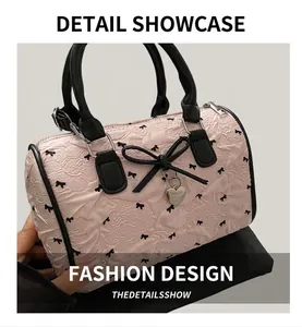 Détail du sac Boston rose avec imprimés nœuds, bordure en cuir noir et breloque cœur argentée
