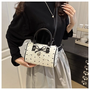 Détail du sac Boston plissé blanc avec imprimés nœuds noirs et pendentif cœur argenté