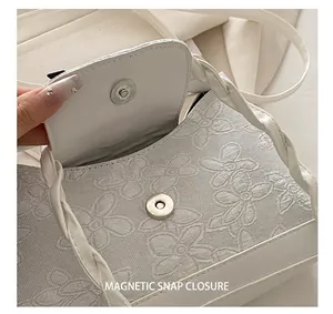 Nahaufnahme der weißen Blumenstickerei und des silbernen Magnetverschlusses der Tasche