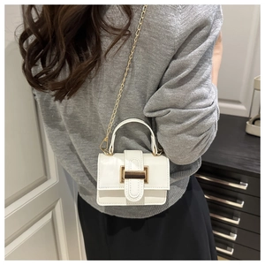 Close-up of white leather mini bag with gold buckle and chain strap on shoulder