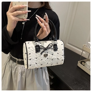 Close-up of a white barrel bag featuring black bow prints and a heart-shaped metal pendant