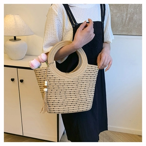 Détail du sac cabas en paille tissée avec poignée ronde, pois noirs et pompon en perles