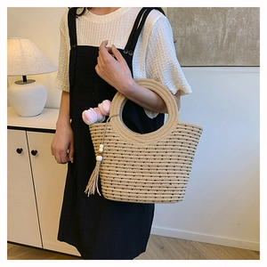 Detalle del bolso tote de paja tejida con lunares negros y colgante de borla decorativo