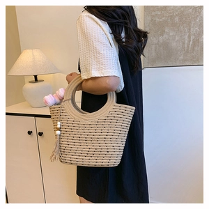 Detalle del bolso tote de paja tejida beige con asa redonda y detalle de borla
