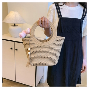 Détail d'un sac en paille tressée avec poignées rondes, rayures noires et pompon