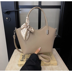 Détail du sac seau en cuir beige avec foulard en soie et breloques en métal en cœur