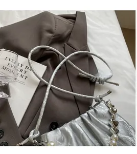 Detail of silver pleated cloud bag with pearl heart charm on brown blazer background