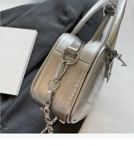 Close-up of silver square bag with metallic texture, chain strap, and key-shaped charm