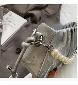 Detailed view of silver pleated handbag with large pearl beads handle and metallic hardware