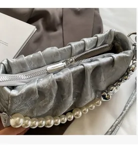 Detail view of smooth metal zipper and pearl heart chain on silver pleated handbag