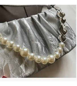 Close-up of silver pleated fabric bag with white pearls handle and heart metal link