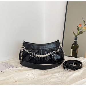 Close-up of black crocodile texture leather bag with heart pearl chain on lace tablecloth