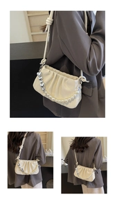 Close-up of beige pleated dumpling bag featuring white pearls and silver heart chain detail