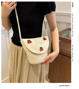 Dettaglio borsa a tracolla in paglia color crema con ricamo ciliegia e patta intrecciata