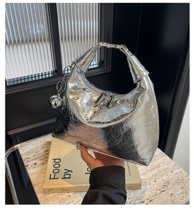 Detailed shot of a silver metallic hobo bag featuring a round ball charm and metal handle
