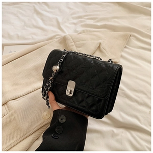 Detail of black quilted crossbody bag with silver metal chain and decorative ball