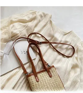Detail of adjustable leather strap and metal buckles on a small straw crossbody bag