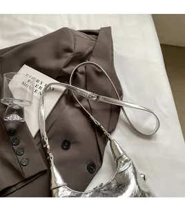 Detail of silver metallic croissant bag with pleated texture on a brown blazer suit
