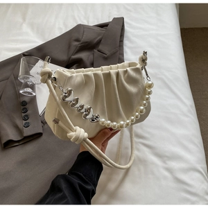 Close-up of cream pleated cloud bag featuring silver heart charms and pearl chain detail