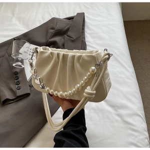 Detailed view of cream pleated cloud bag featuring pearl and heart-shaped metal chain charm