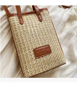 Detail of hand-woven straw crossbody bag featuring brown leather trim and embossed tag