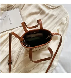 Close-up of woven straw bucket bag showing interior space with a mobile phone and leather strap