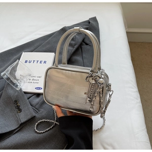 Detail view of silver square handbag with metallic texture and key-shaped charm