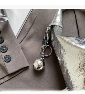 Detail of silver crinkled handbag featuring a metallic ball charm on a brown blazer