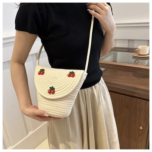 Dettaglio di una borsa a secchiello intrecciata bianco crema con ricami di ciliegie 3D