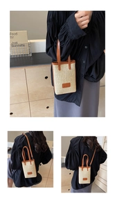 Close-up of woven straw handbag featuring premium dark brown leather handles and stitching