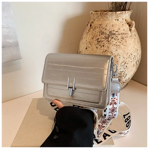 Detail of silver textured square bag with horizontal embossing and designer wide strap