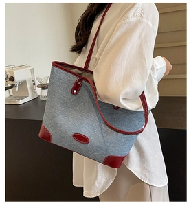 Detail of blue denim tote bag with red leather trim and white contrast stitching on shoulder strap