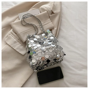Detailed view of silver sequin bucket bag with metal chain strap on white blazer