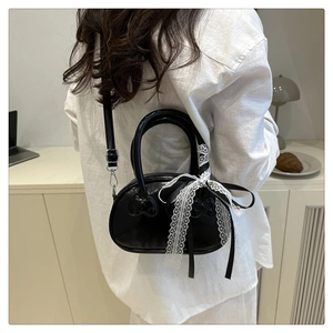Detail of black glossy PU leather handbag with embossed bows and white lace ribbon