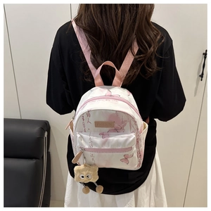 Detail view of mini white backpack featuring pink butterfly prints and plush monster charm