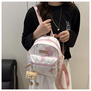 Detail of white butterfly print backpack with pink straps and a brown plush charm