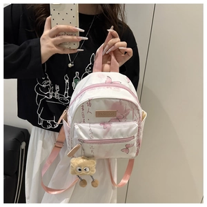 Detail eines weißen Mini-Rucksacks mit rosa Schmetterlingsdruck und Plüschmonster-Anhänger