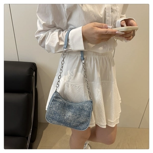 Blue glitter fabric baguette bag with silver chain strap worn by a model in a room